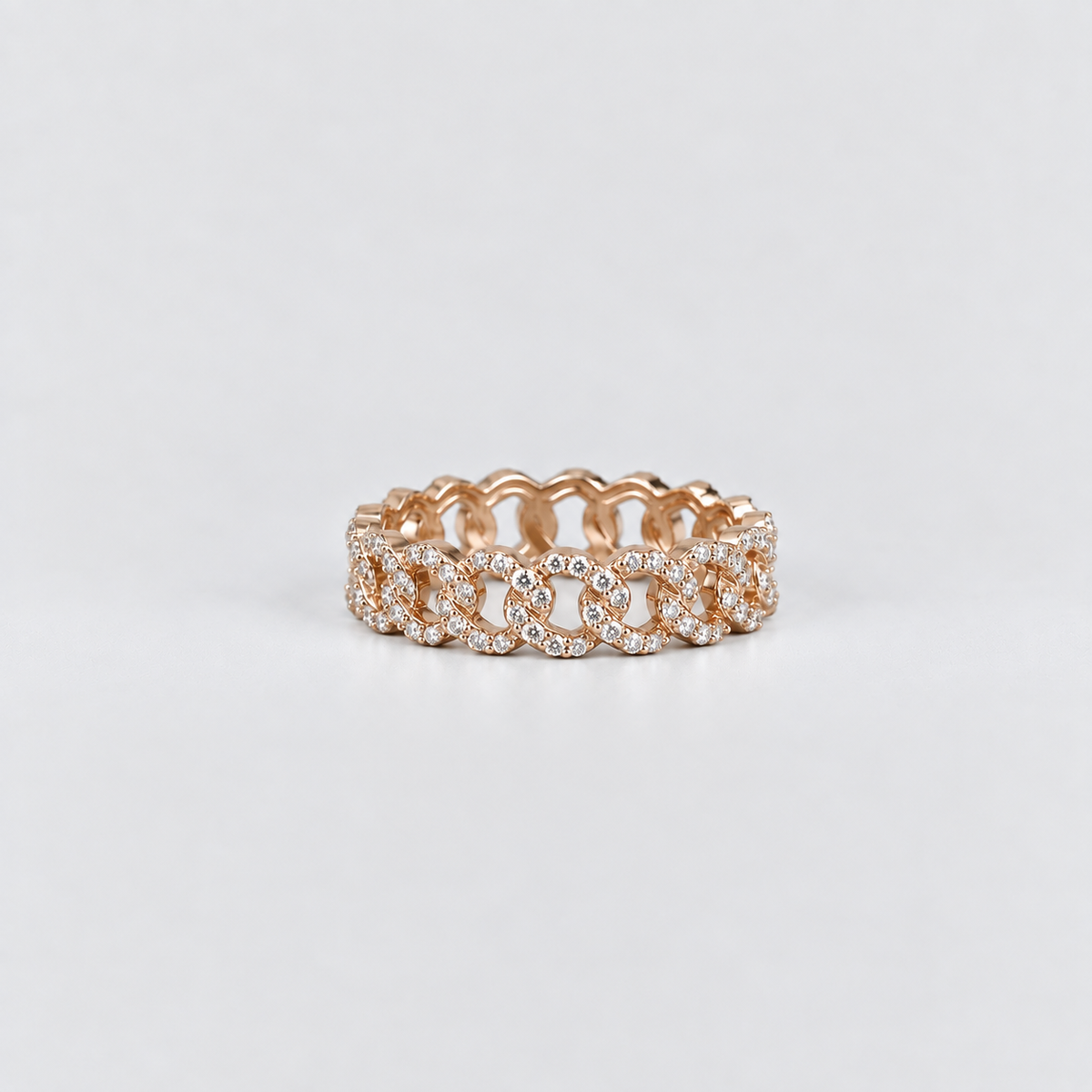 A rose gold eternity ring featuring a continuous pattern of interlocking floral motifs paved with small clear stones, set against a clean light gray background.