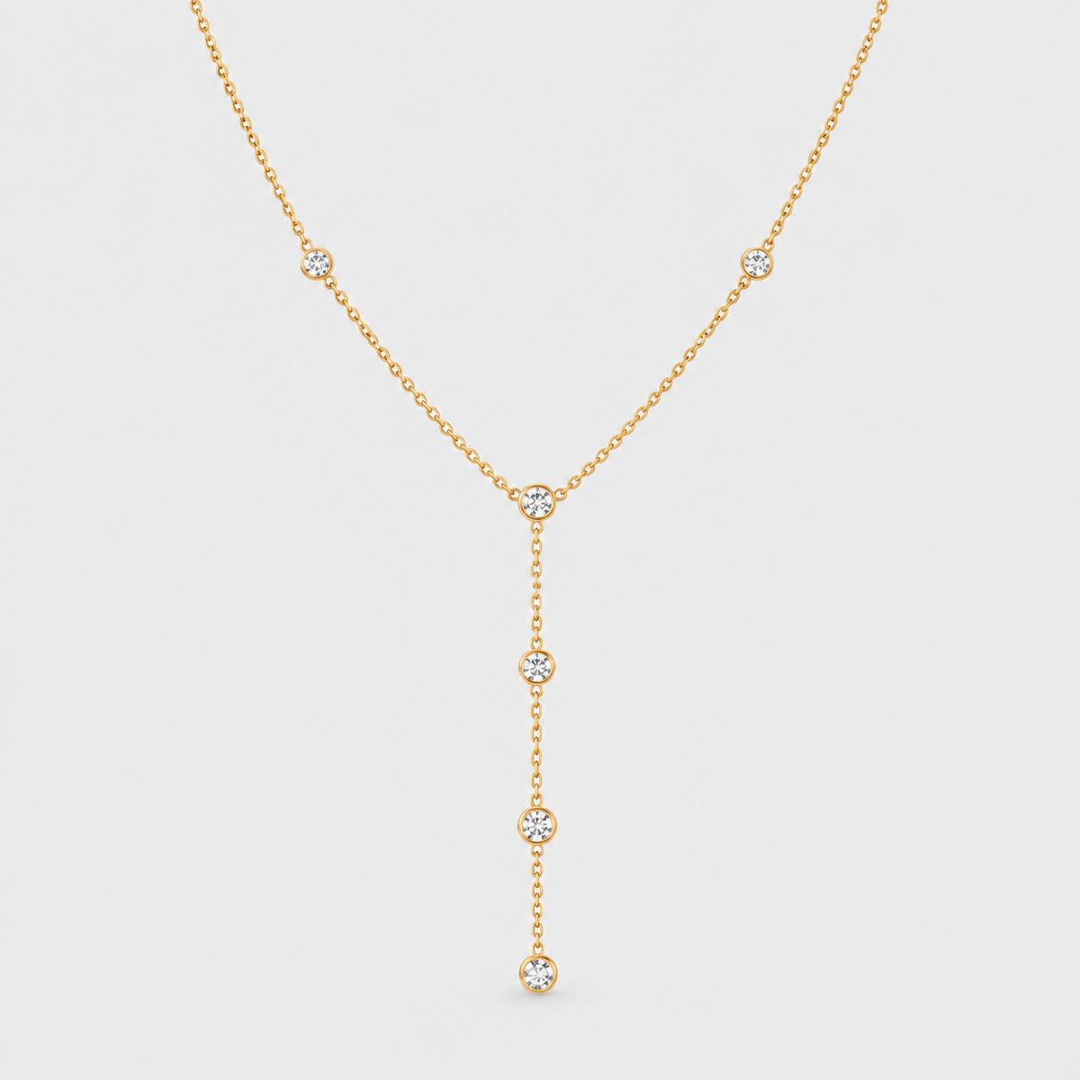 A delicate gold Y-necklace featuring five small round-cut clear gemstones set along the chain and hanging drape, displayed against a light gray background.