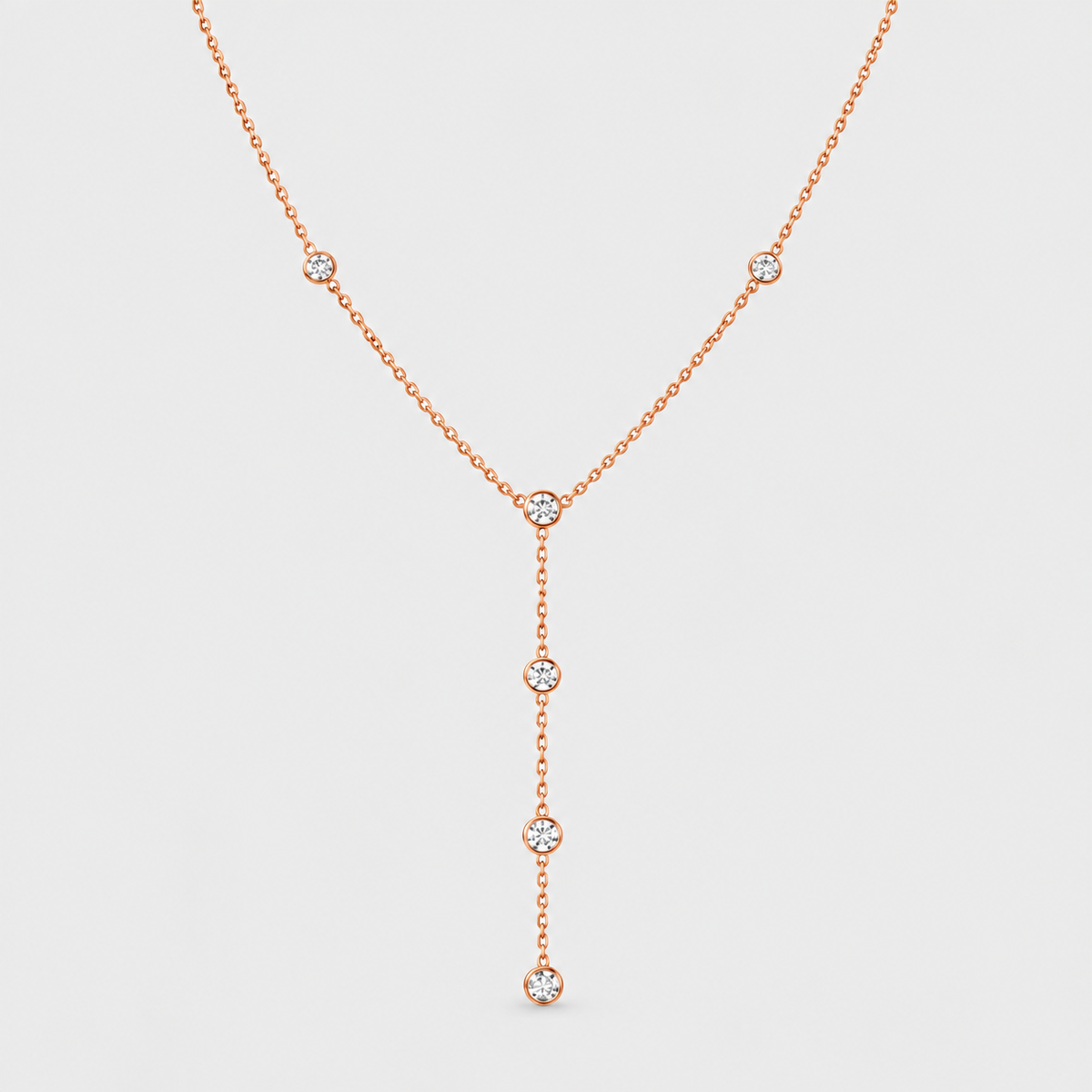 A delicate rose gold Y-necklace featuring five small round-cut clear gemstones set along the chain, displayed against a solid light gray background.