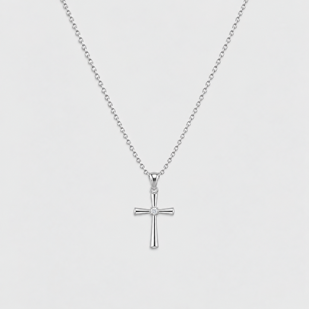 A silver cross pendant necklace with a small clear gemstone at the center, suspended from a delicate silver ball chain against a light gray background.