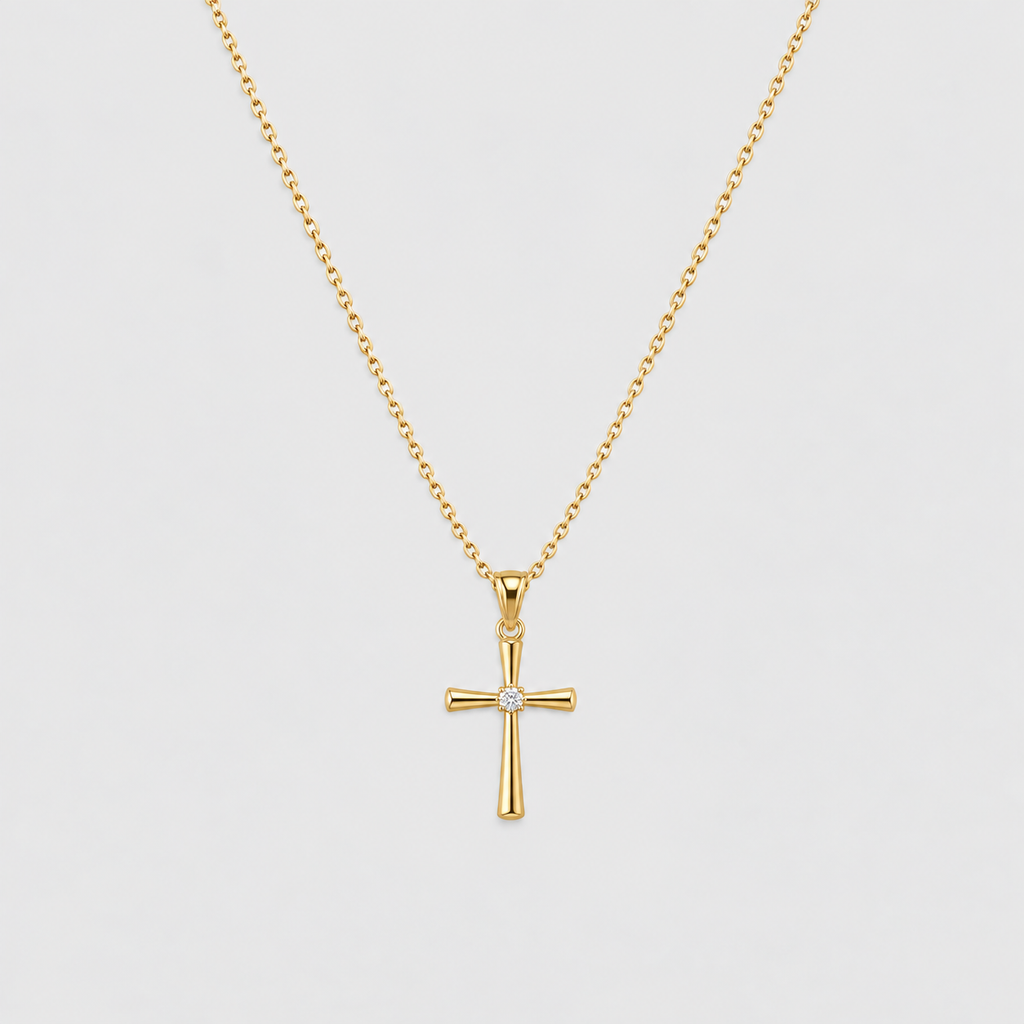 A gold cross pendant necklace with a small clear gemstone at the center, suspended from a delicate gold chain against a light gray background.