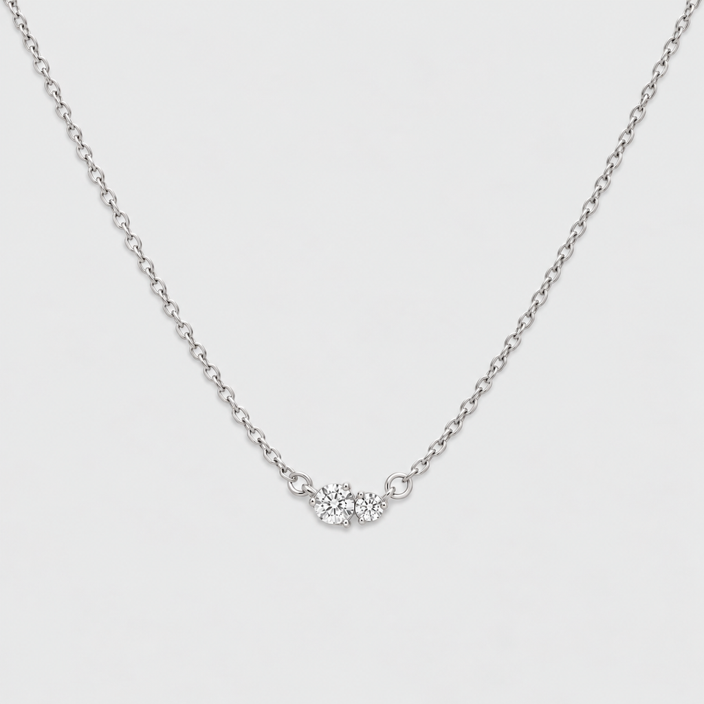 A delicate silver chain necklace featuring a small central cluster of clear gemstones, photographed against a clean, light gray background.