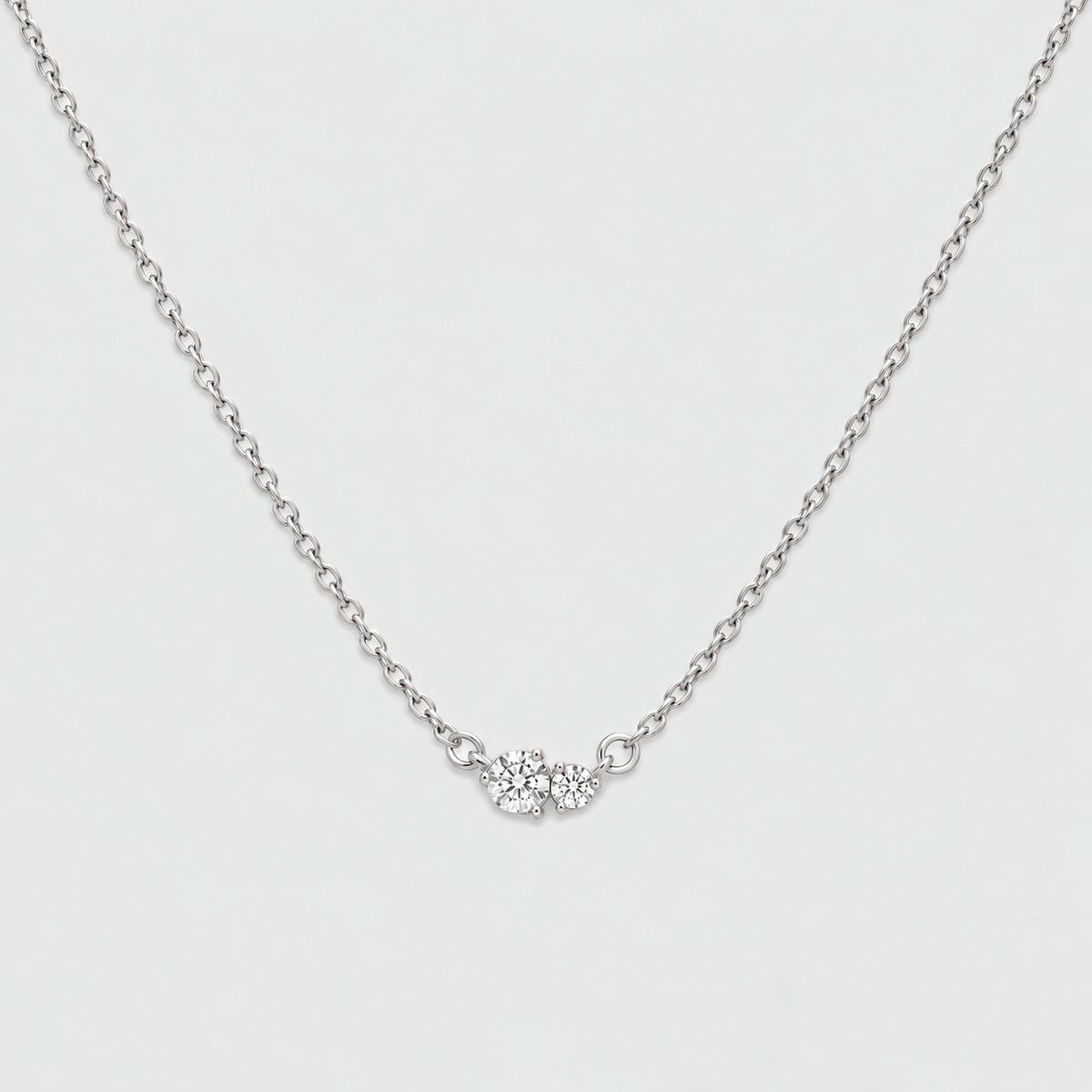 A delicate silver chain necklace featuring a small central cluster of clear gemstones, photographed against a clean, light gray background.