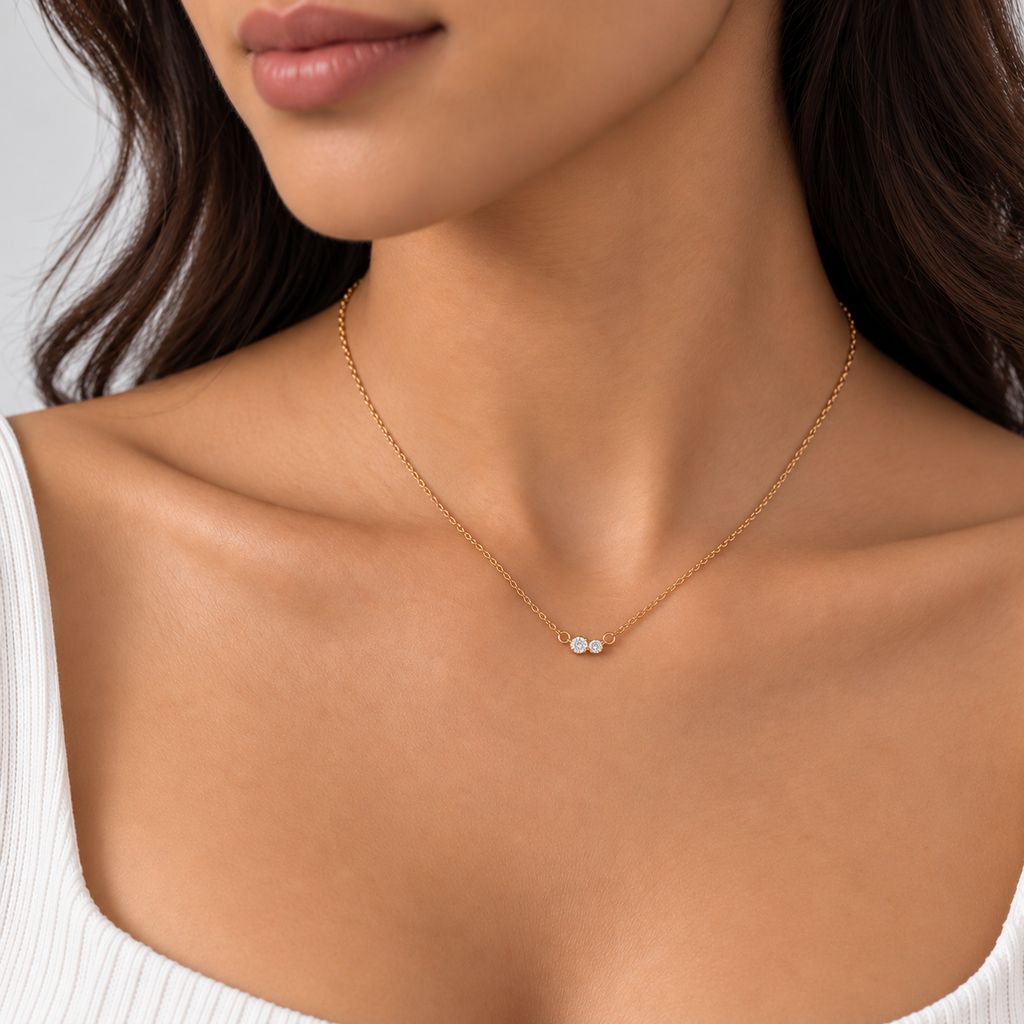 A close-up of a woman wearing a delicate gold chain necklace with a small three-stone silver pendant, styled with a white ribbed top.