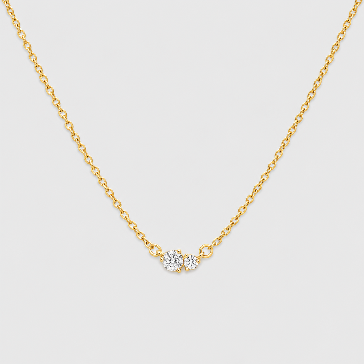 A delicate gold chain necklace featuring a small central cluster of three clear round-cut gemstones in a gold setting, displayed against a light gray background.