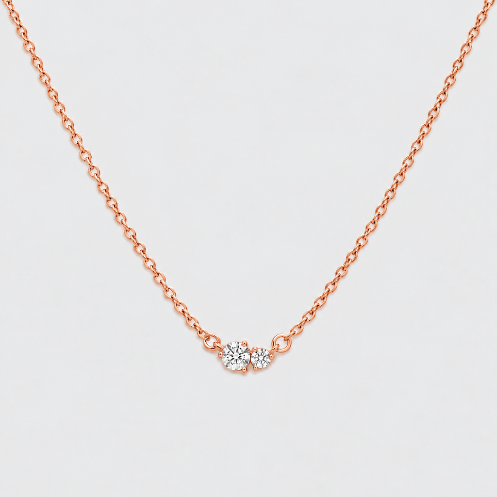 A delicate rose gold chain necklace with a small central cluster of clear gemstones, displayed against a clean, light gray background.