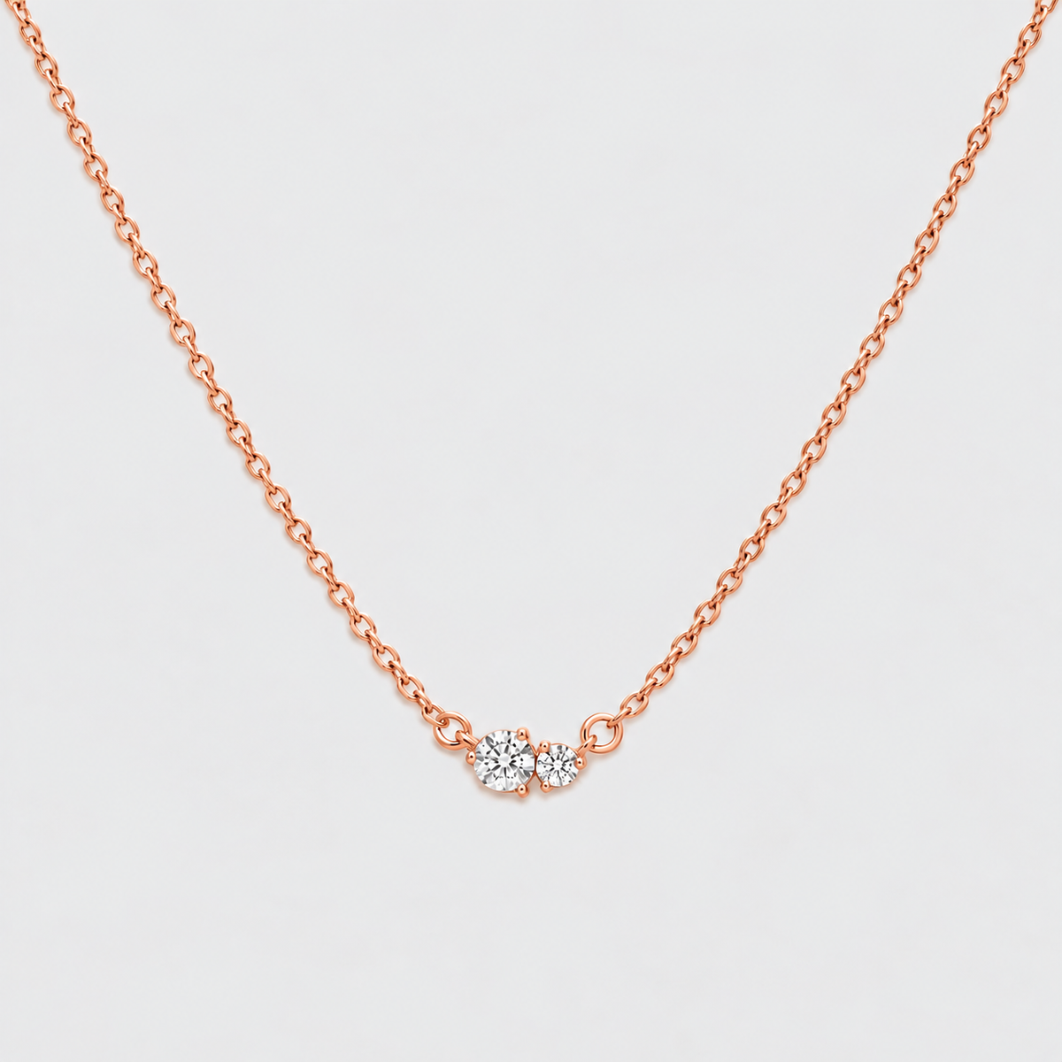 A delicate rose gold chain necklace with a small central cluster of clear gemstones, displayed against a clean, light gray background.