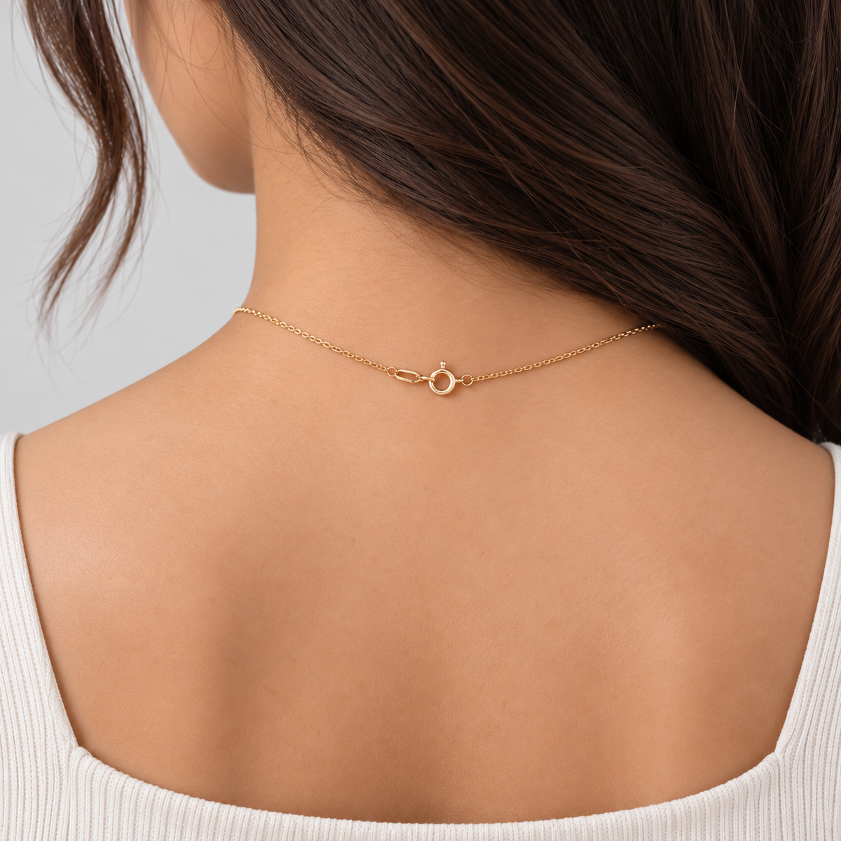 A delicate gold chain necklace with a small open circle pendant, shown worn on the back of a woman's neck over a white ribbed top.