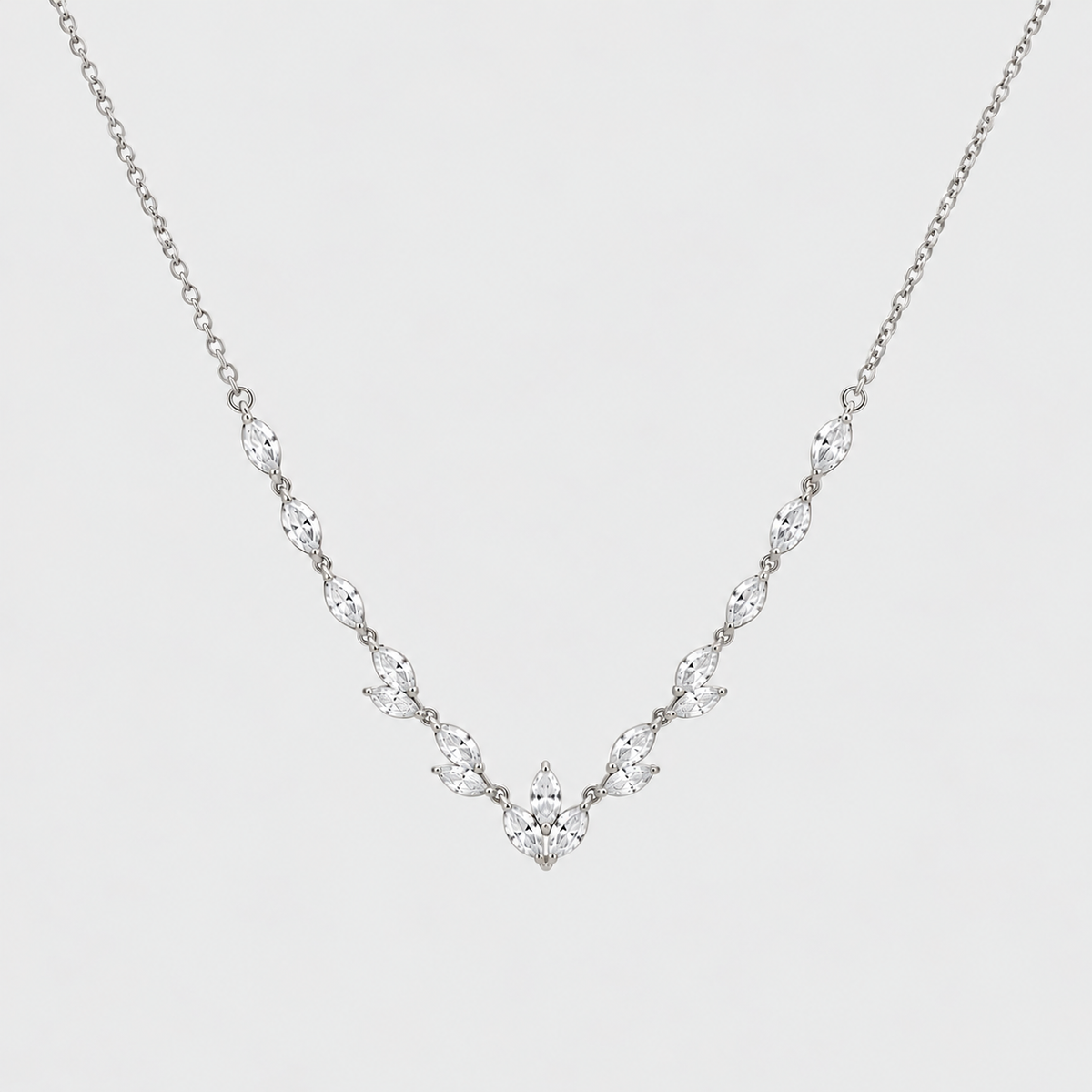 A delicate silver-toned necklace featuring a V-shaped arrangement of marquise-cut clear stones on a fine chain, set against a plain light gray background.