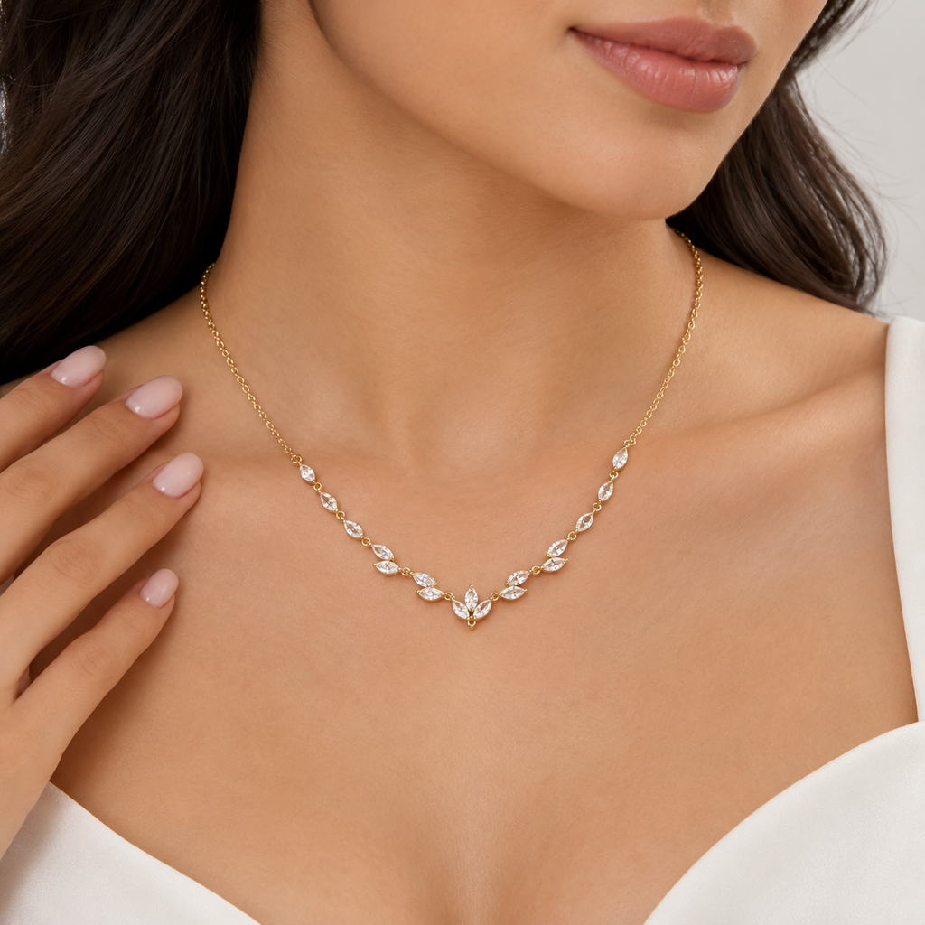 A close-up of a woman wearing a delicate gold leaf necklace with clear crystals, styled with a white top.