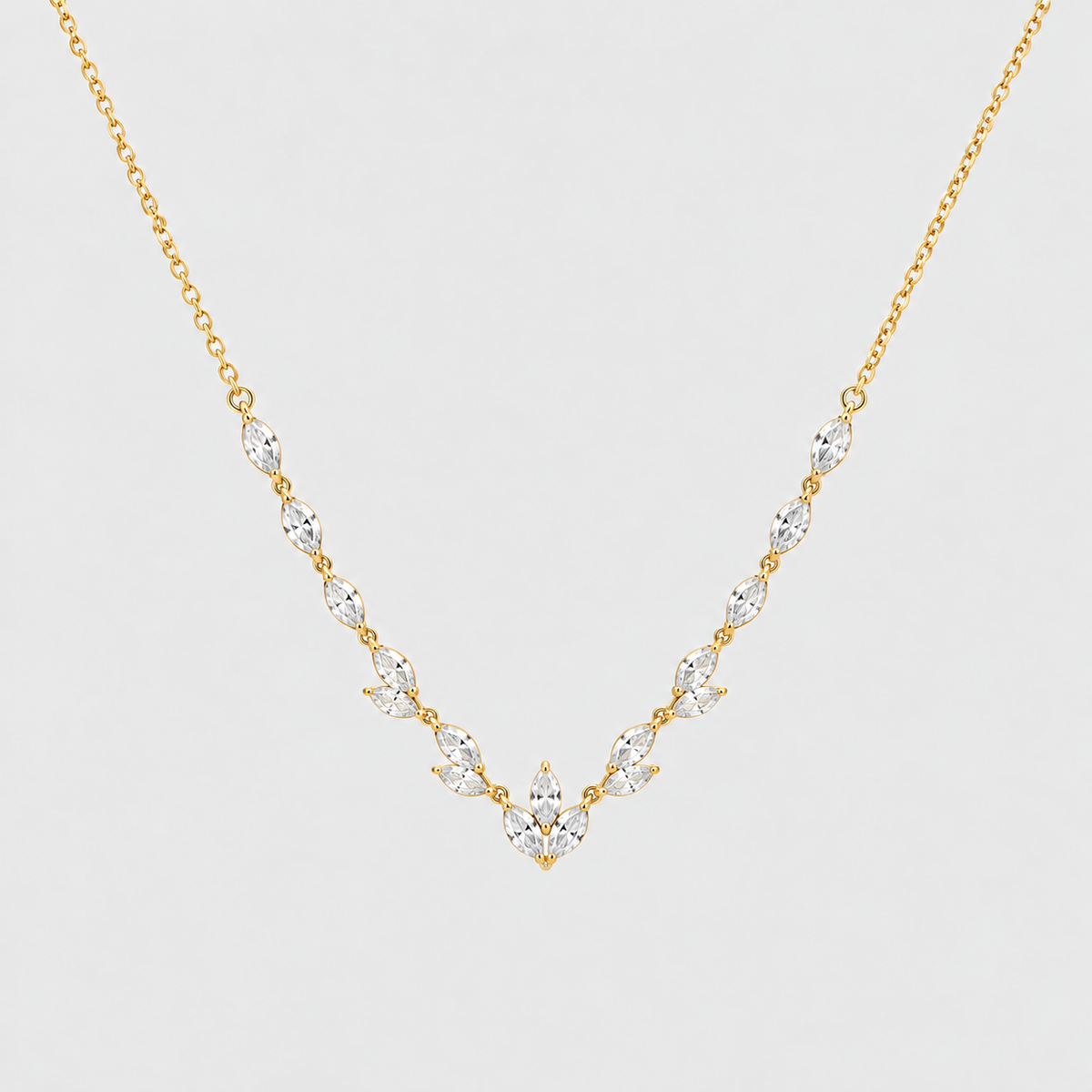A delicate gold necklace featuring a V-shaped arrangement of marquise-cut clear gemstones on a light gray background.