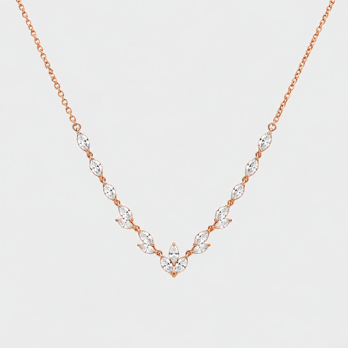 A delicate rose gold necklace featuring a V-shaped arrangement of marquise-cut clear gemstones on a light gray background.