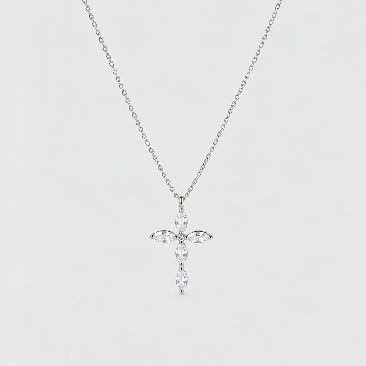 A silver cross pendant necklace adorned with clear marquise-cut and round-cut stones, suspended from a delicate silver chain against a light gray background.