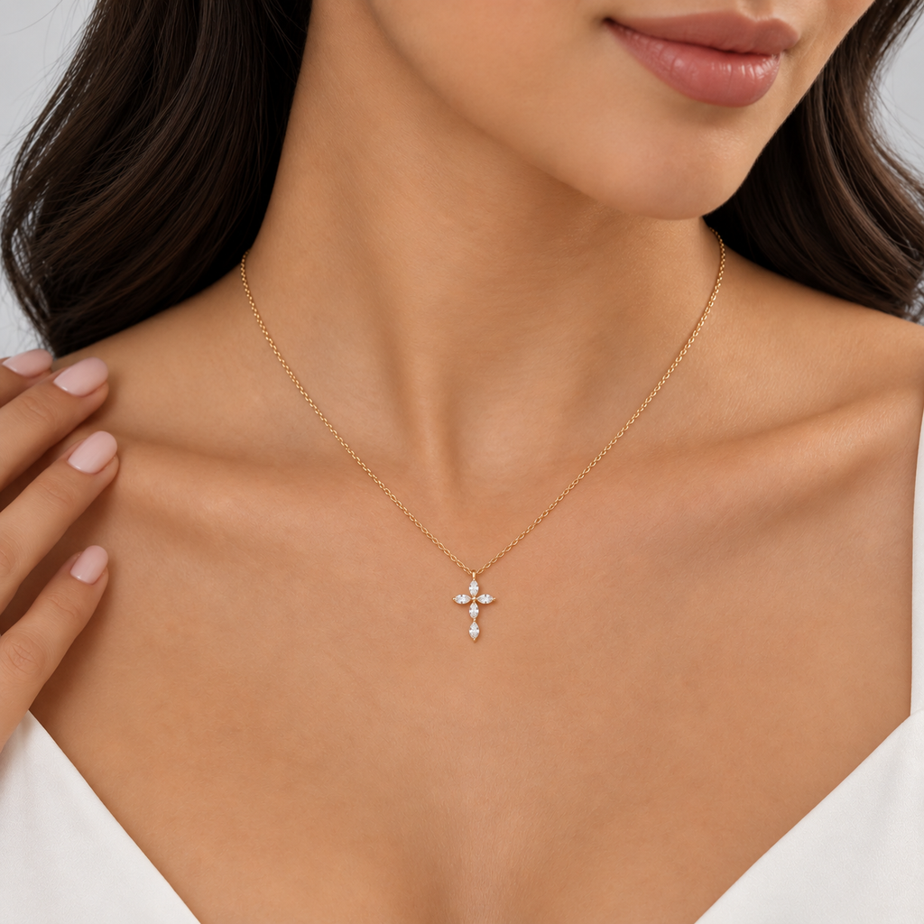 A close-up of a woman wearing a delicate gold cross pendant necklace with small clear stones, shown on her neck and upper chest.
