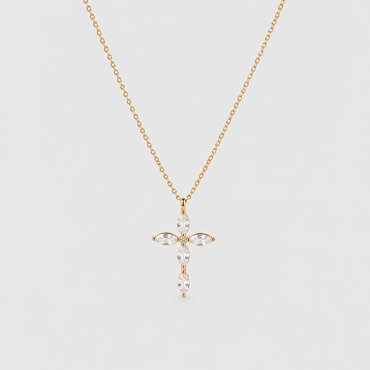 A delicate gold chain necklace with a cross-shaped pendant adorned with marquise-cut clear gemstones, displayed against a solid light gray background.