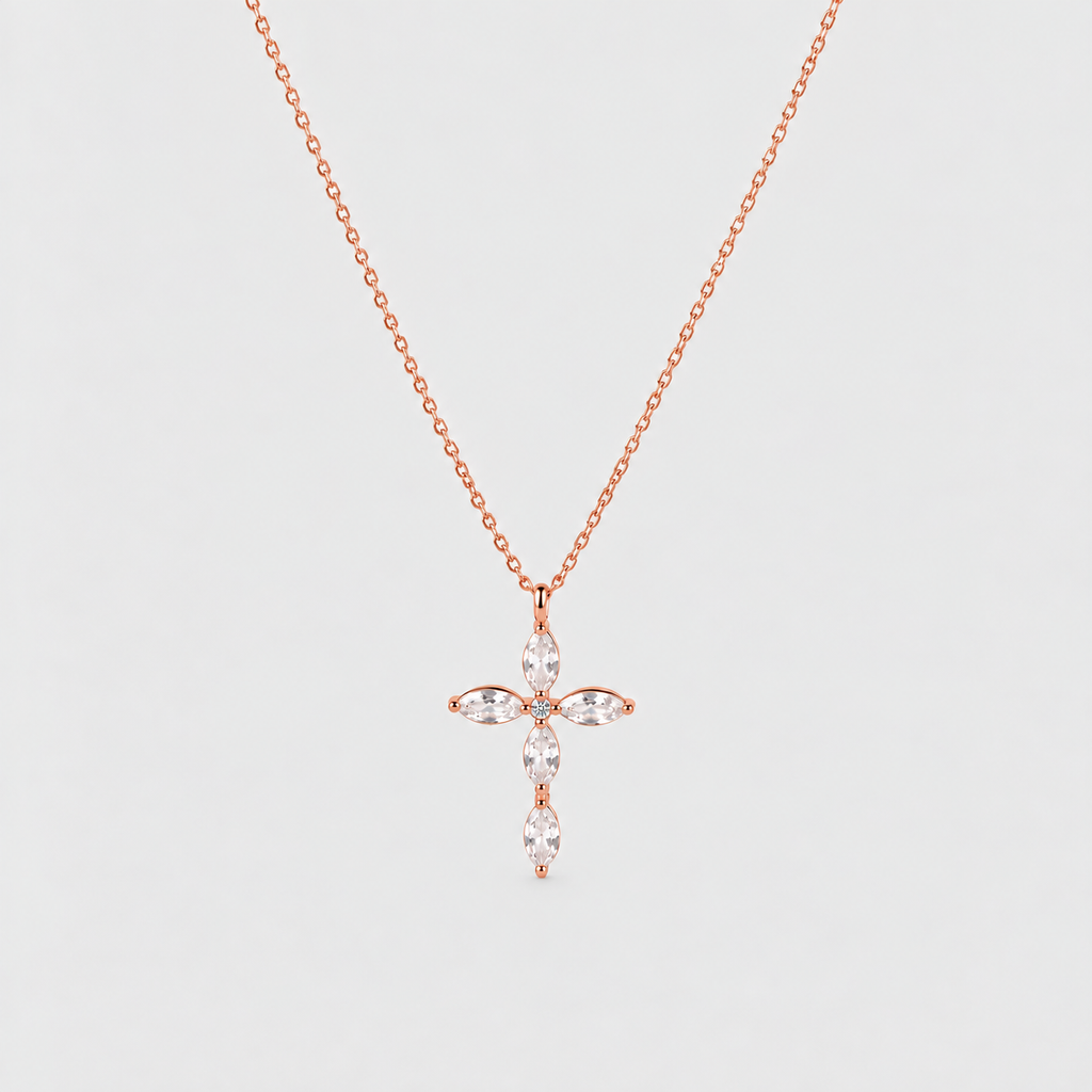 A delicate rose gold chain necklace featuring a cross-shaped pendant adorned with marquise-cut clear gemstones, set against a solid light gray background.
