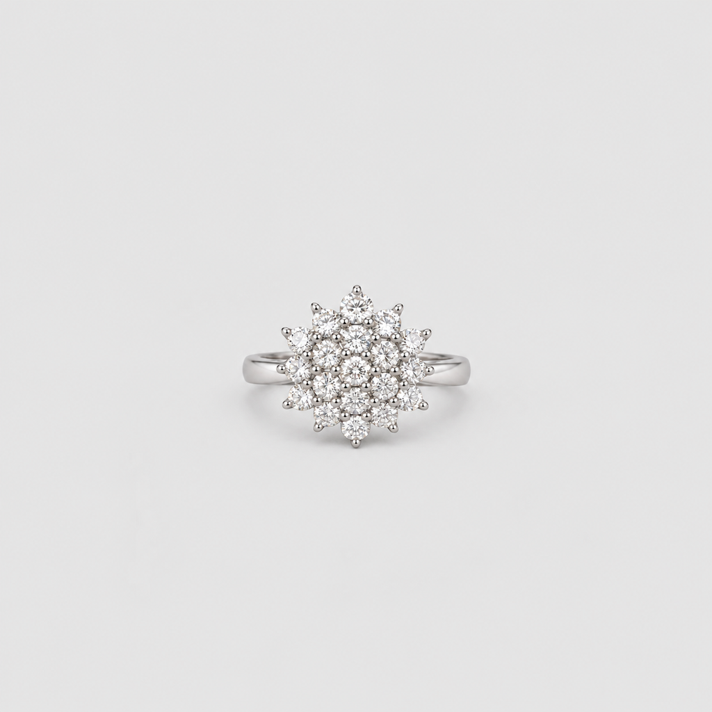 A silver-toned ring featuring a circular cluster of small clear gemstones in a starburst or snowflake-like arrangement, centered on a light gray background.