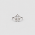A silver-toned ring featuring a circular cluster of small clear gemstones in a starburst or snowflake-like arrangement, centered on a light gray background.
