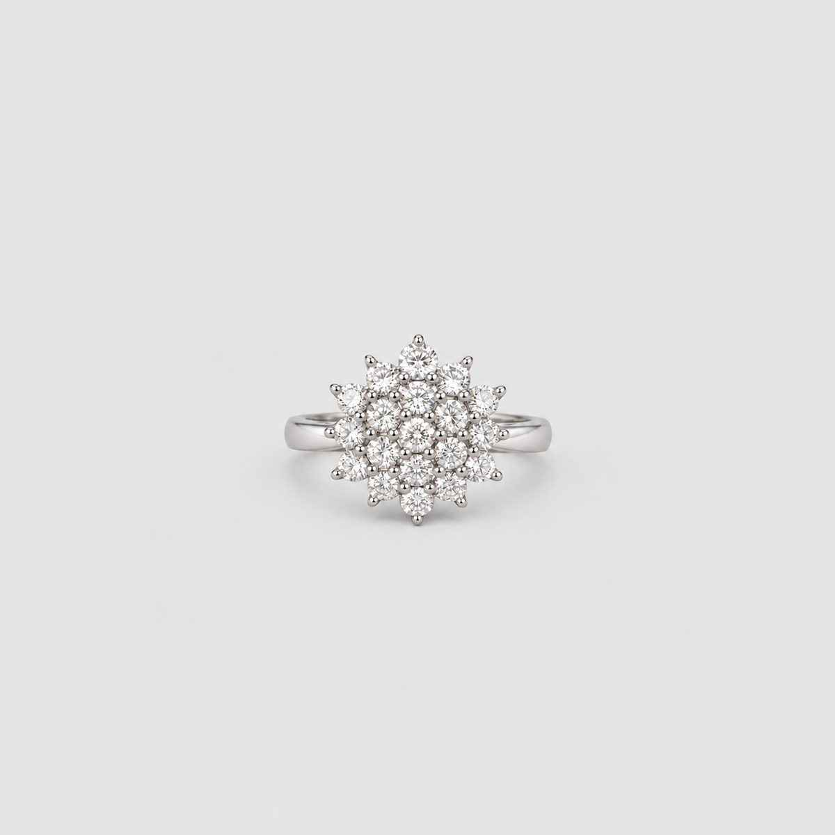 A silver-toned ring featuring a circular cluster of small clear gemstones in a starburst or snowflake-like arrangement, centered on a light gray background.