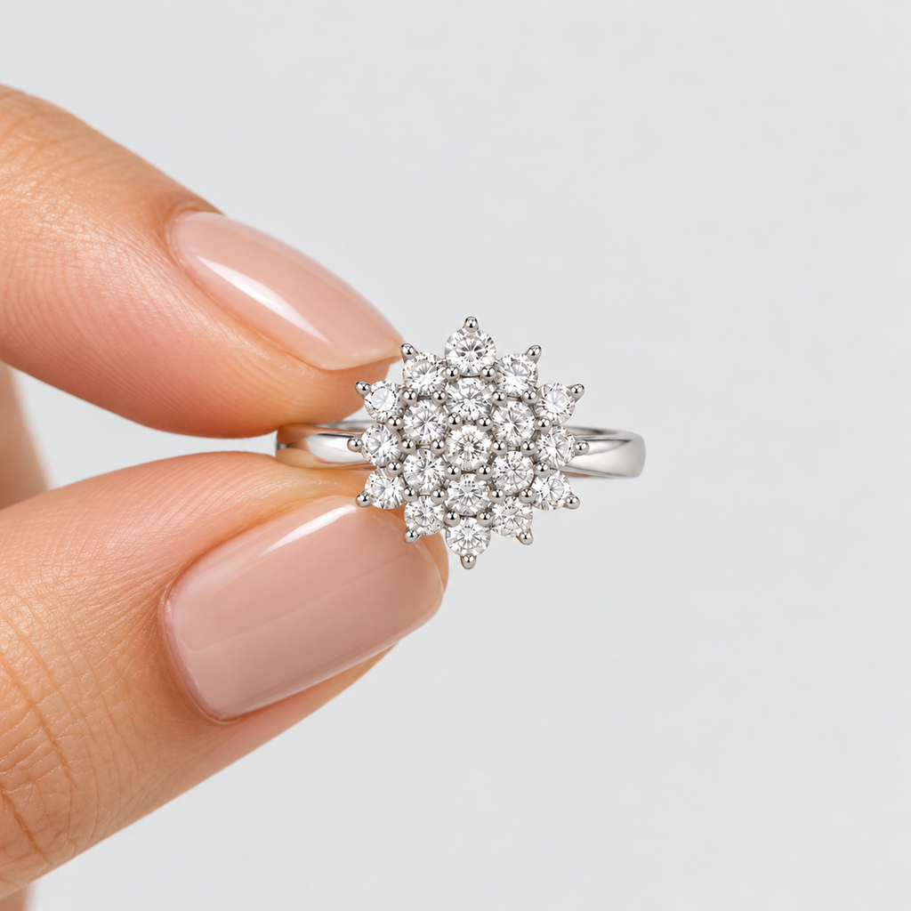 A silver-toned ring with a round cluster of clear gemstones held between fingers against a light gray background.