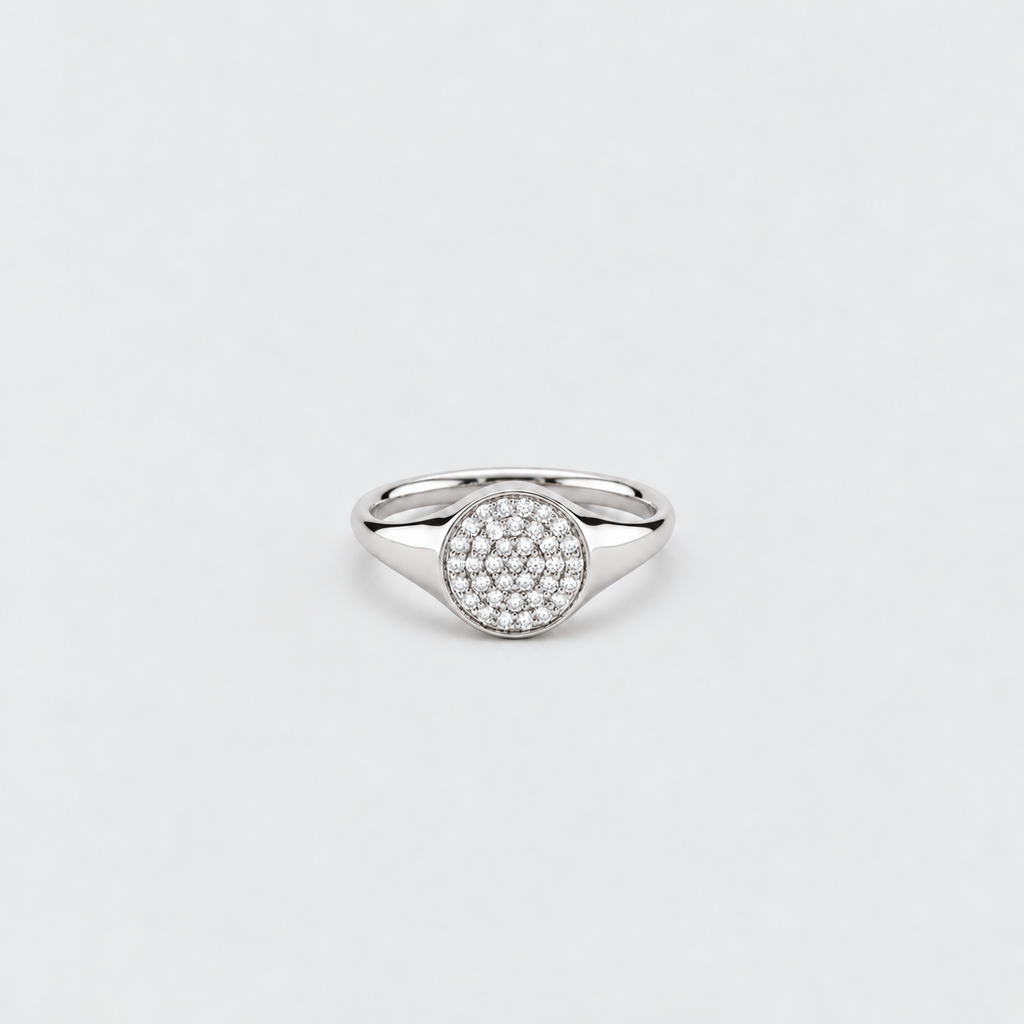 A silver-toned signet ring featuring a round pavé-set stone center, photographed on a clean, light gray background.