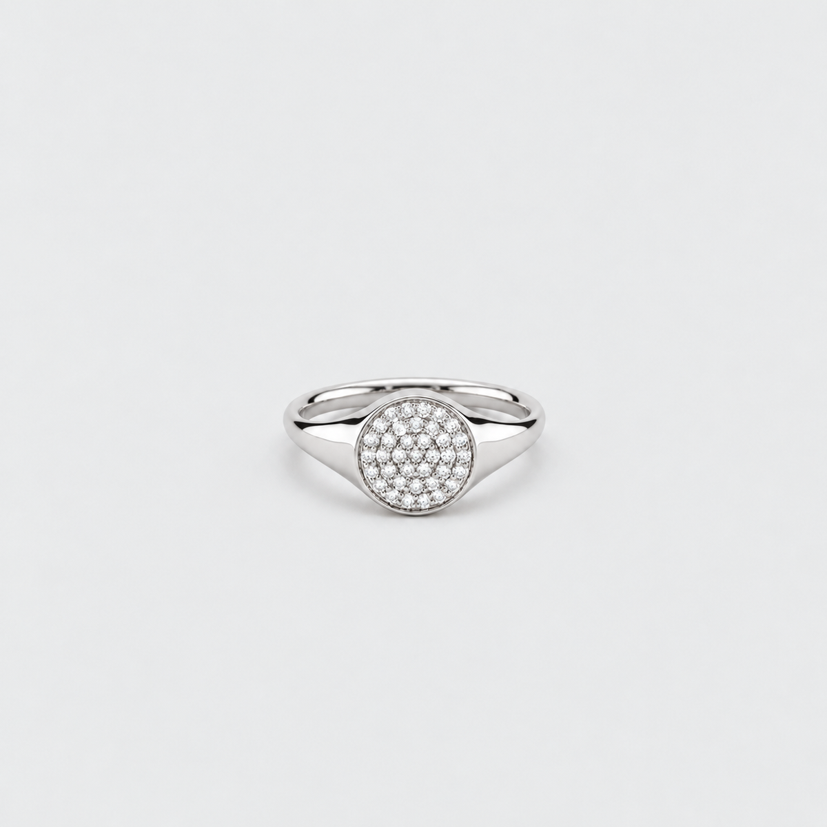 A silver-toned signet ring featuring a round pavé-set stone center, photographed on a clean, light gray background.