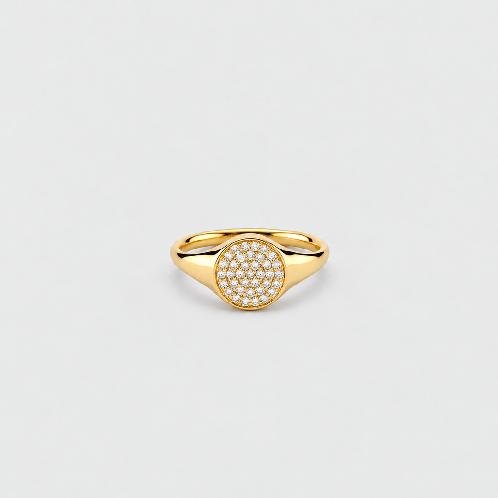 A gold signet-style ring with a circular pavé-set face, photographed on a clean light gray background.
