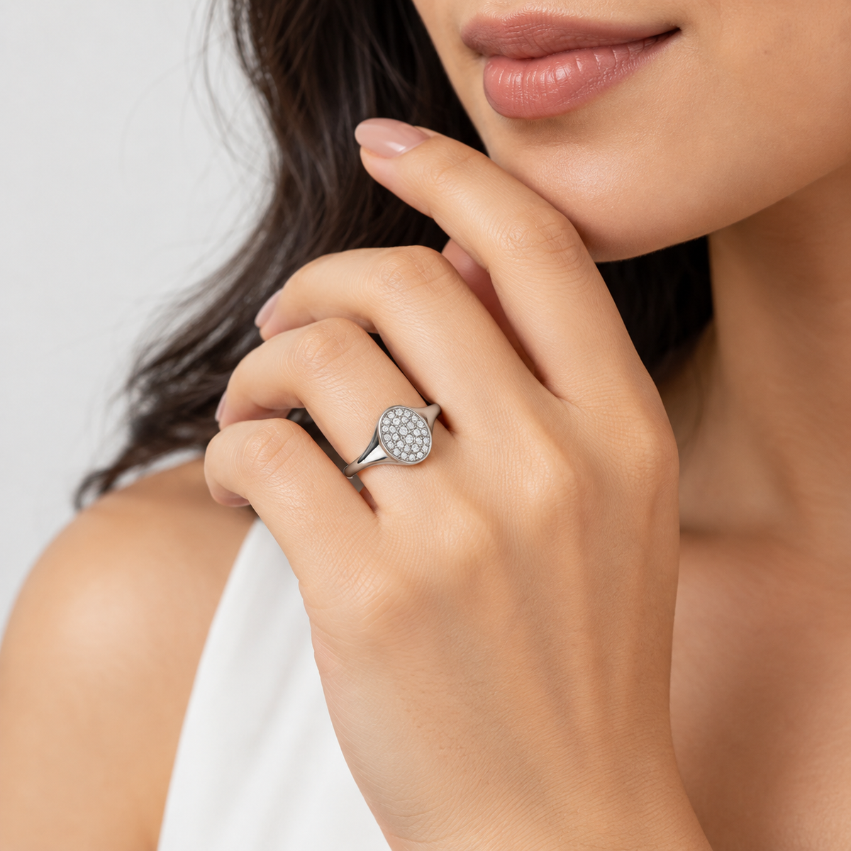 A close-up lifestyle shot of a woman wearing a silver ring with a round pavé diamond setting on her finger.