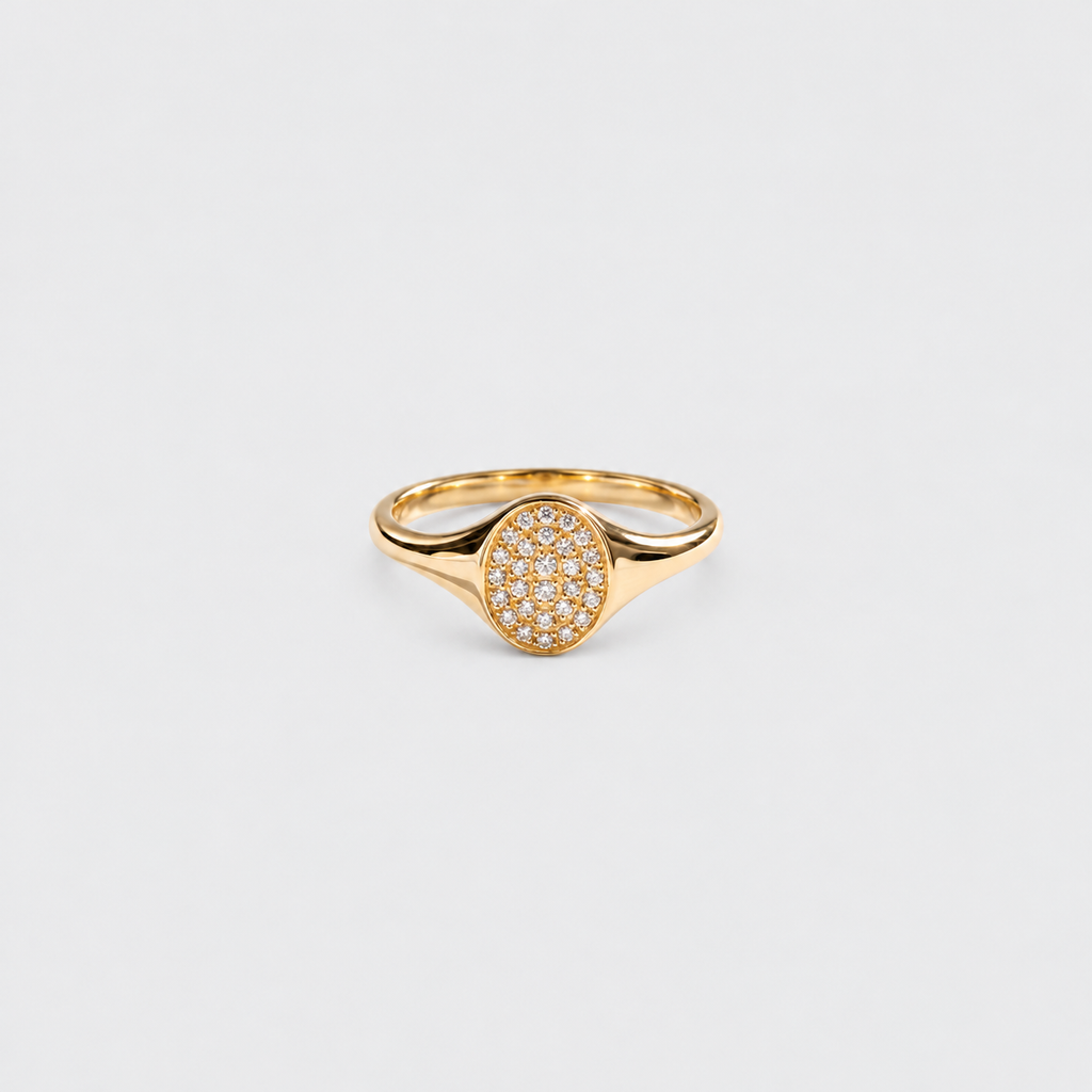 A gold signet-style ring with an oval pavé setting, photographed on a clean light gray background.