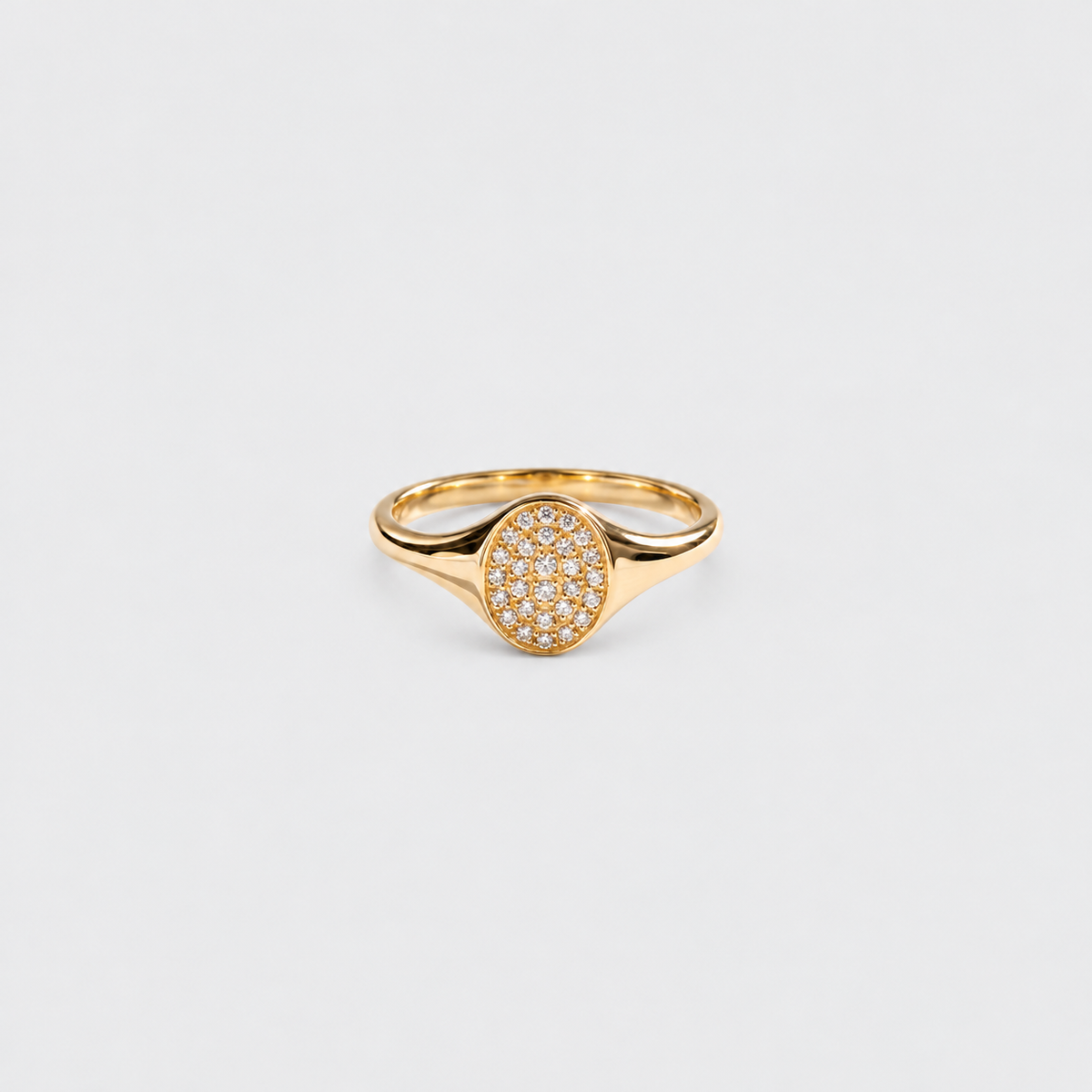 A gold signet-style ring with an oval pavé setting, photographed on a clean light gray background.