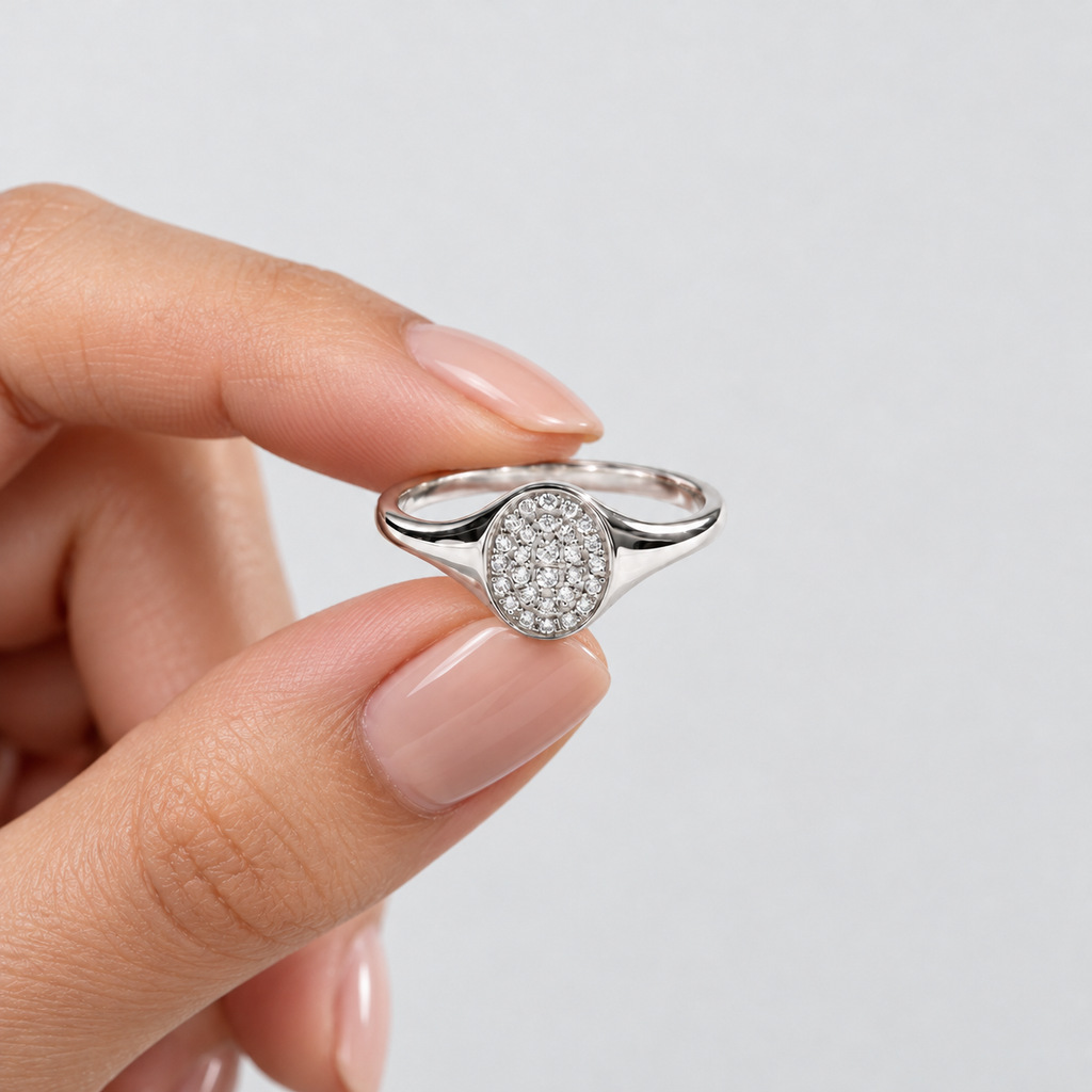 A silver ring with a round pavé-set clear stone held between fingers against a light gray background.