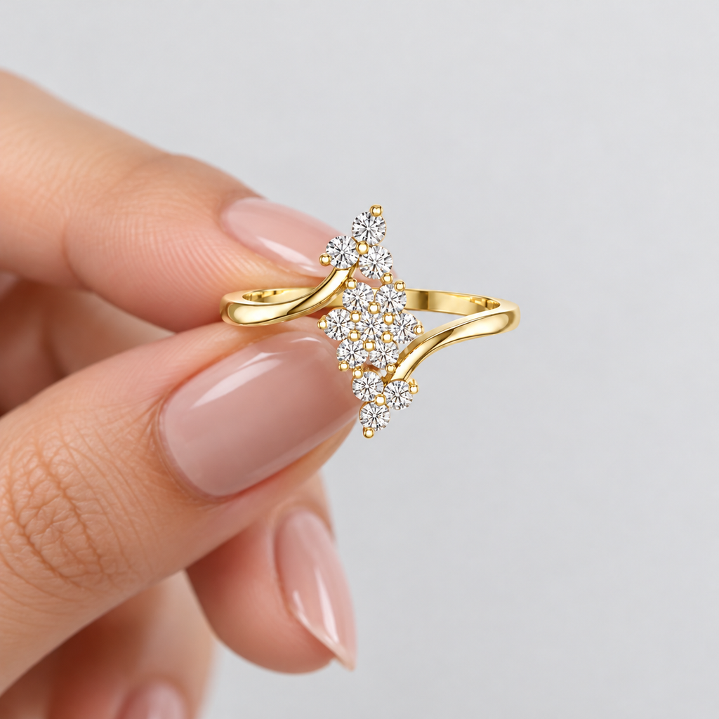 A gold ring with a floral cluster of clear pavé stones, held between fingers against a soft light gray background.