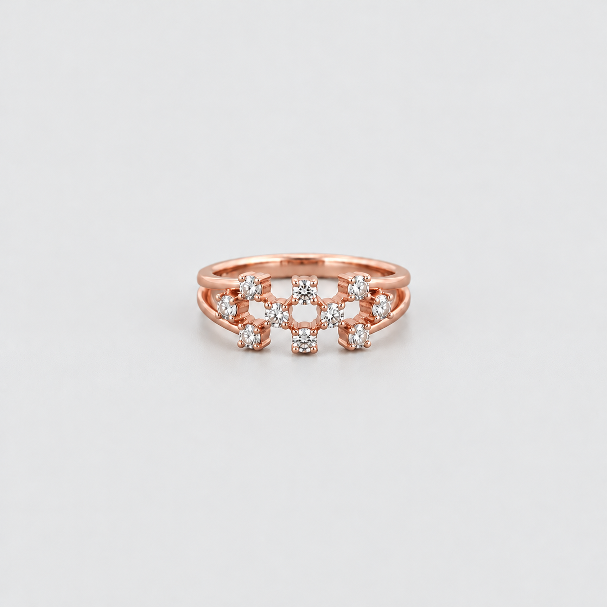 A rose gold ring with a multi-band design featuring small clear gemstones, photographed on a clean light gray background.