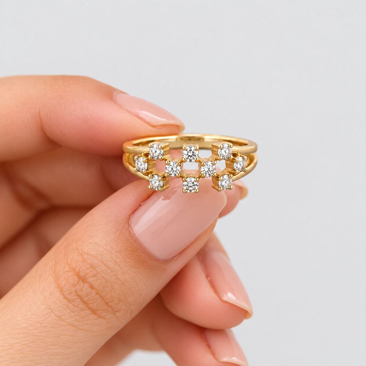A gold ring with a row of small clear gemstones, held between fingers against a light gray background.