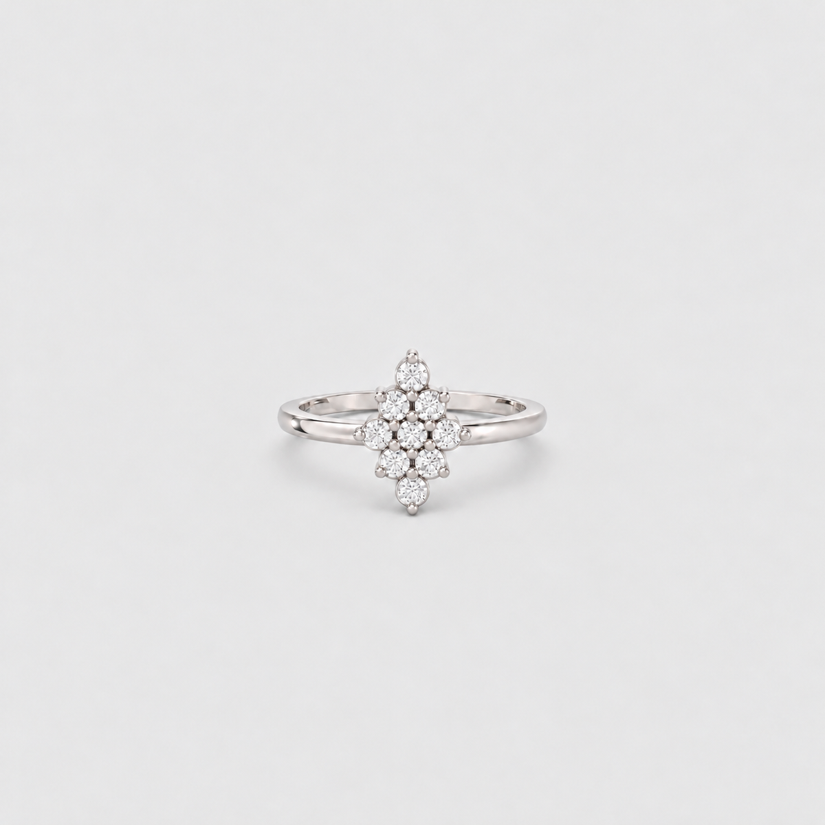 A silver-toned ring featuring a central cluster of small clear gemstones arranged in a floral or starburst pattern, set on a plain light gray background.