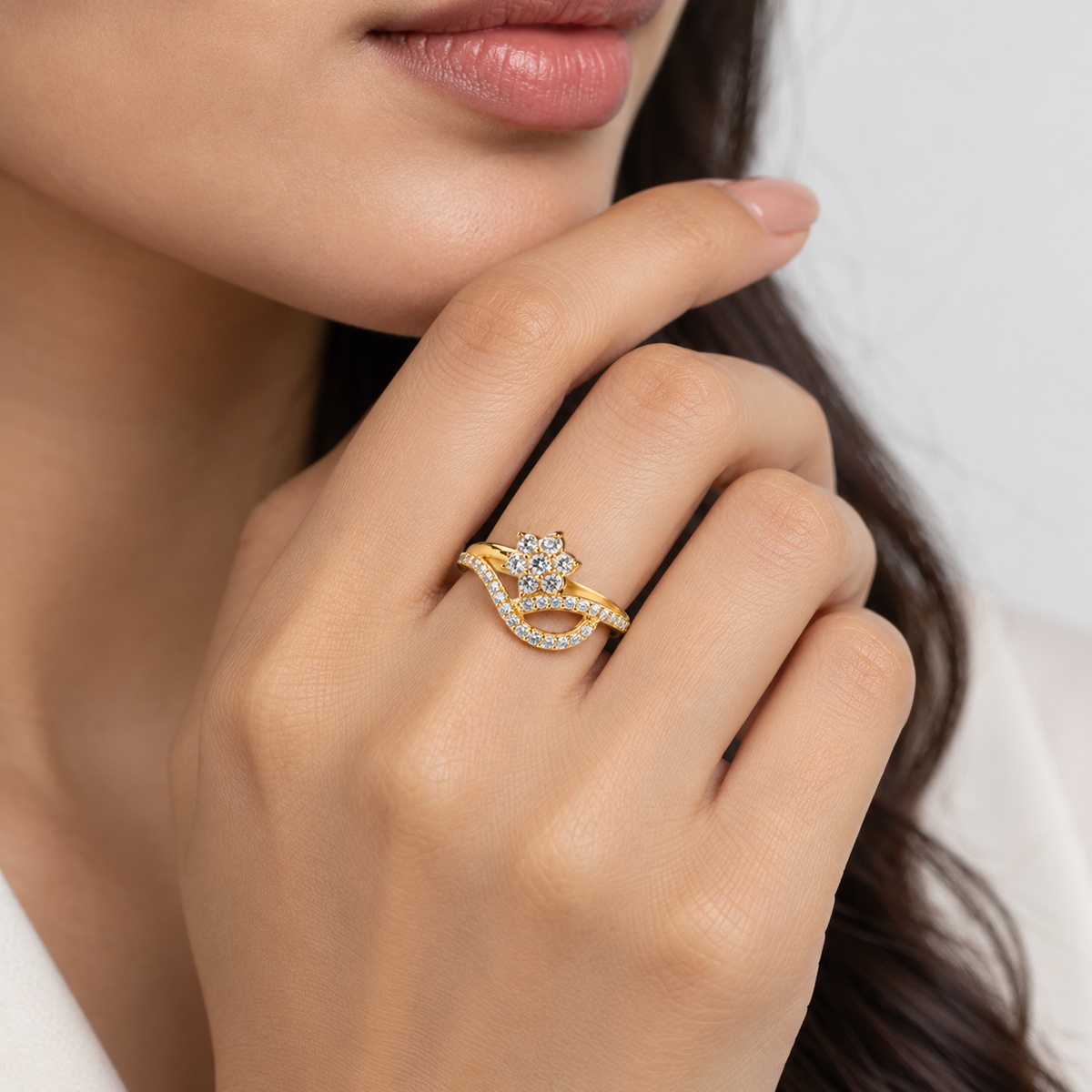 A close-up of a woman's hand wearing a gold ring with a diamond-encrusted bow design, set against a soft light gray background.
