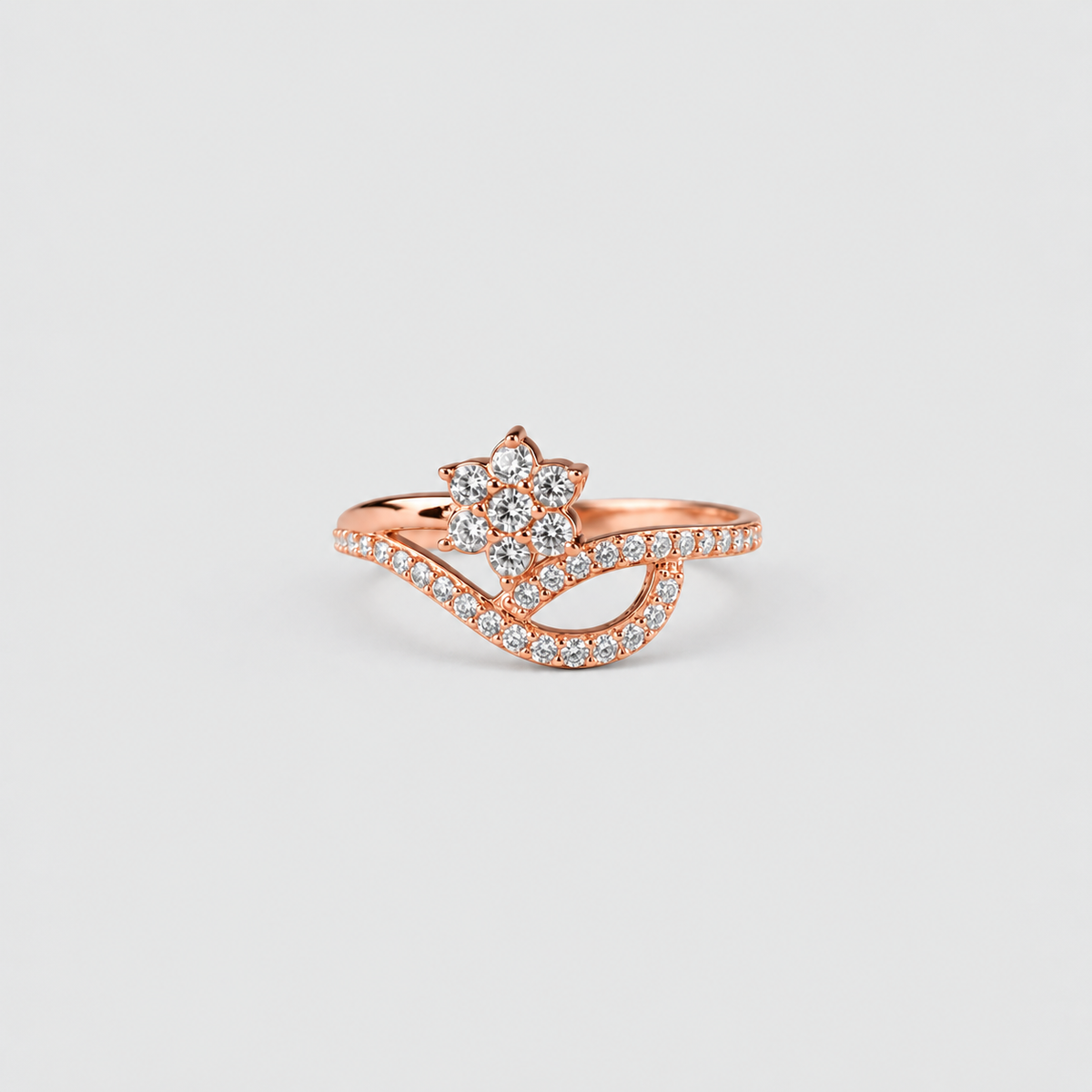A rose gold ring with a flower-shaped cluster of clear stones and a wavy pavé band, shown on a light gray background.