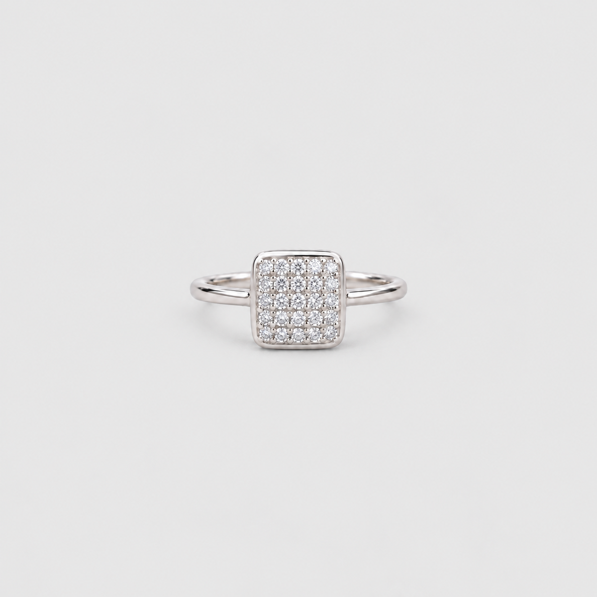 A silver square pavé ring with a pave-set diamond center and a slim band, shown on a light gray background.