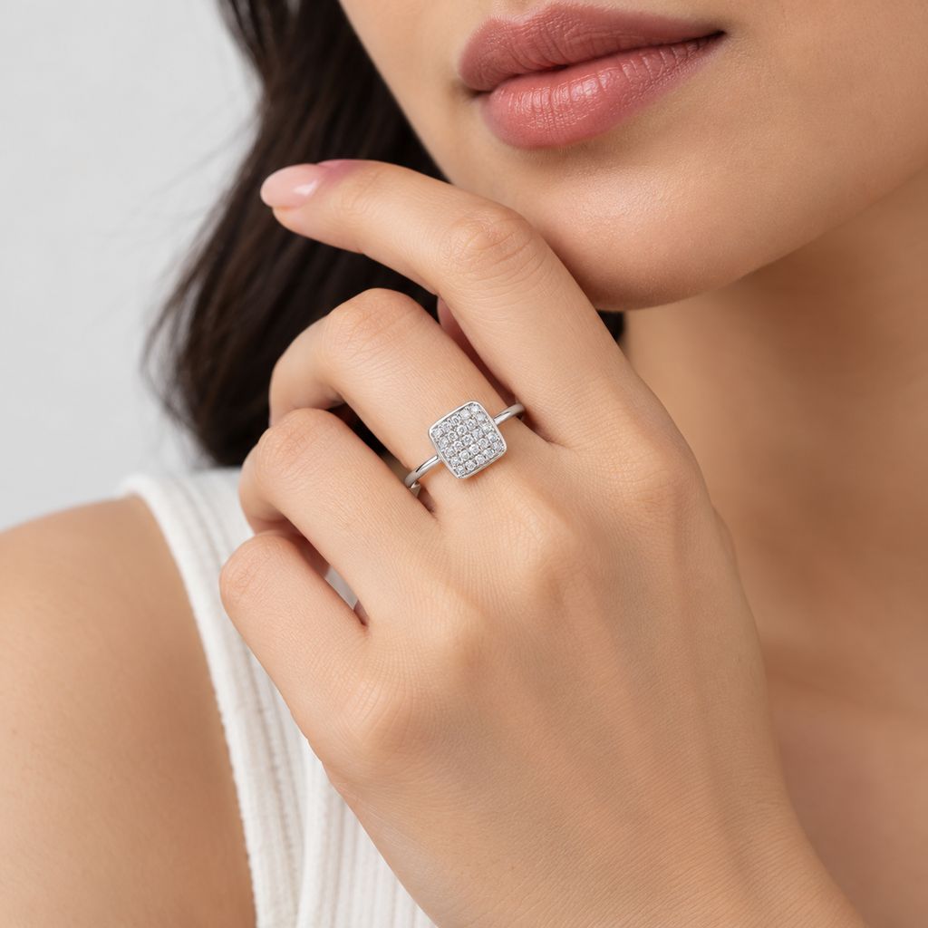A close-up lifestyle shot of a model wearing a silver square ring set with small clear stones on her finger.
