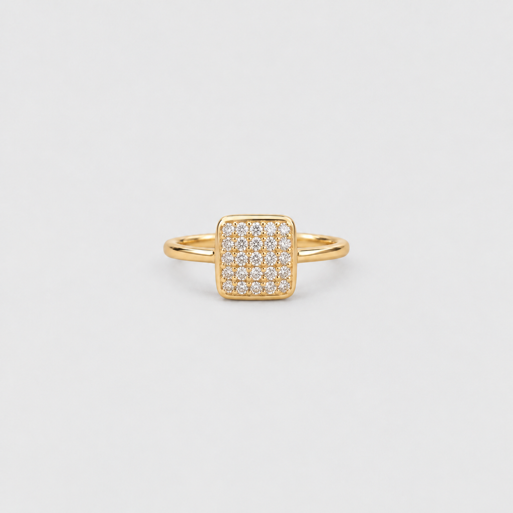 A gold square ring featuring a pavé-set diamond center, photographed on a clean, light gray background.