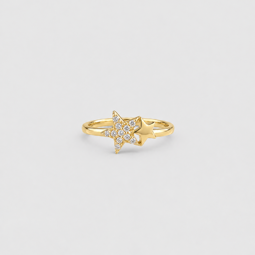 A gold ring featuring a star-shaped pavé setting with clear stones and a polished gold accent star beside it, shown on a light gray background.
