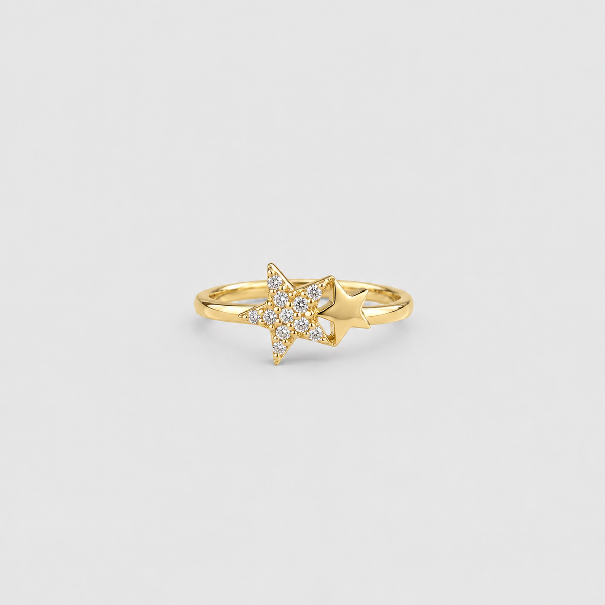 A gold ring featuring a star-shaped pavé setting with clear stones and a polished gold accent star beside it, shown on a light gray background.