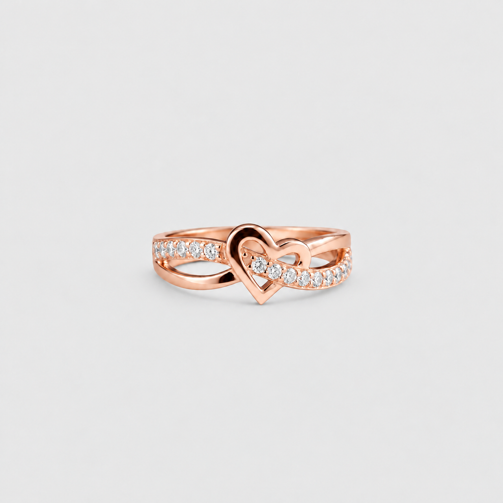 A rose gold ring featuring a central heart design with pavé-set clear stones on the band, shown against a light gray background.
