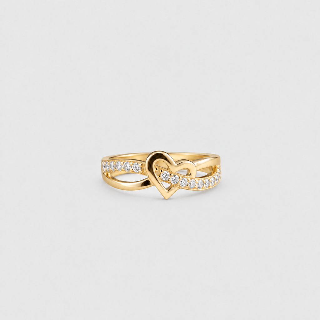 A yellow gold ring featuring a central open heart design with pavé-set clear stones along the band, photographed on a clean light gray background.