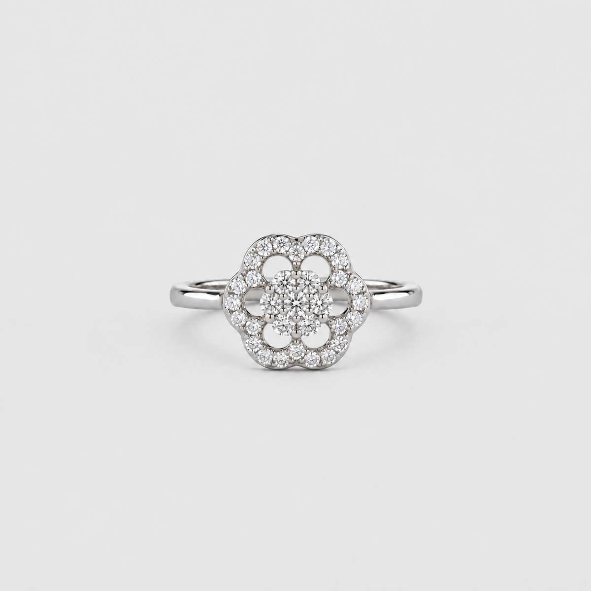 A silver-toned flower cluster ring with a central round diamond surrounded by a halo of smaller diamonds, set on a plain light gray background.