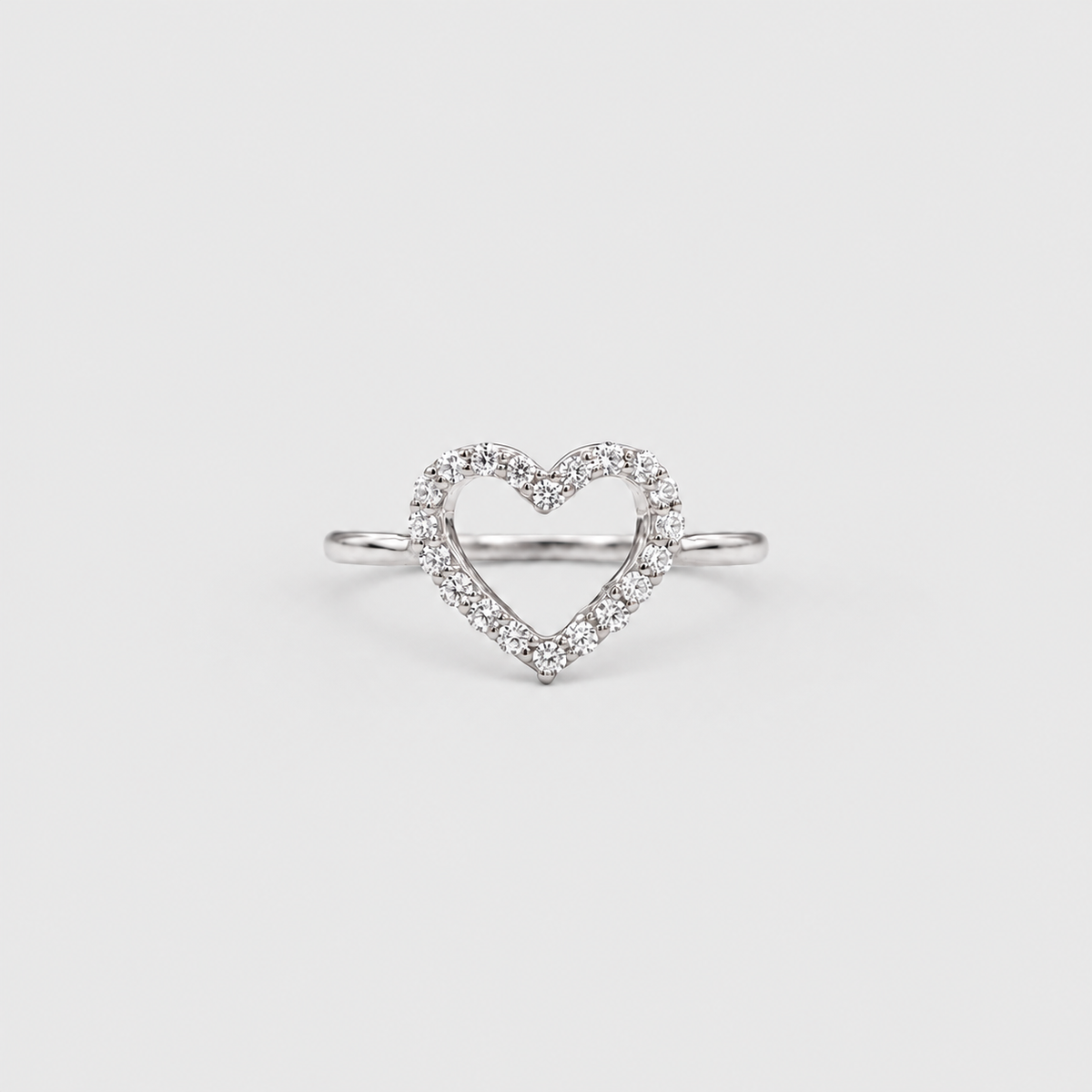 A silver heart-shaped ring with a pavé diamond border, photographed on a clean, light gray background.