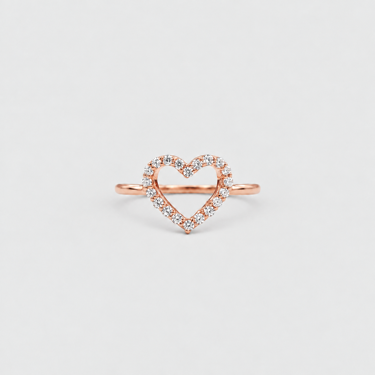 A rose gold open heart ring with a delicate border of small clear stones, centered on a light gray background.