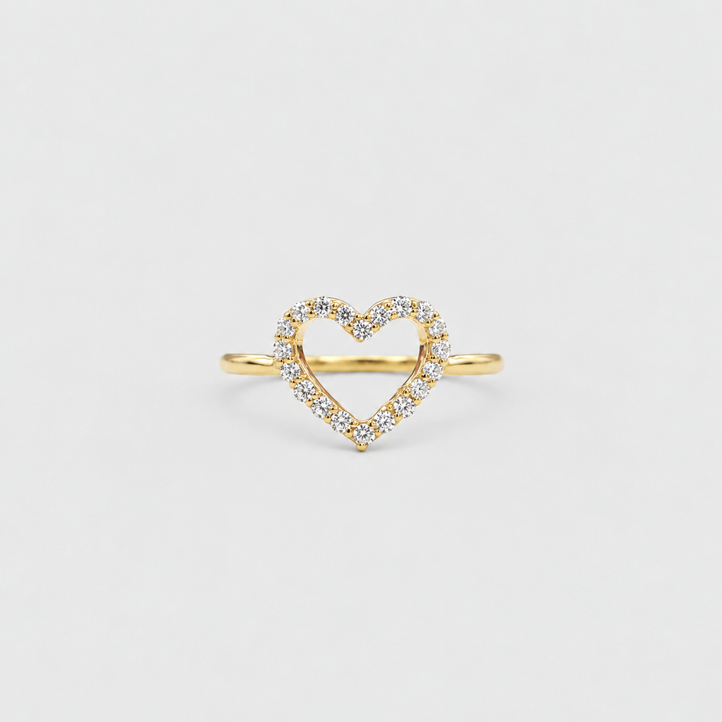 A delicate yellow gold ring featuring an open heart-shaped center paved with small clear stones, set against a solid light gray background.