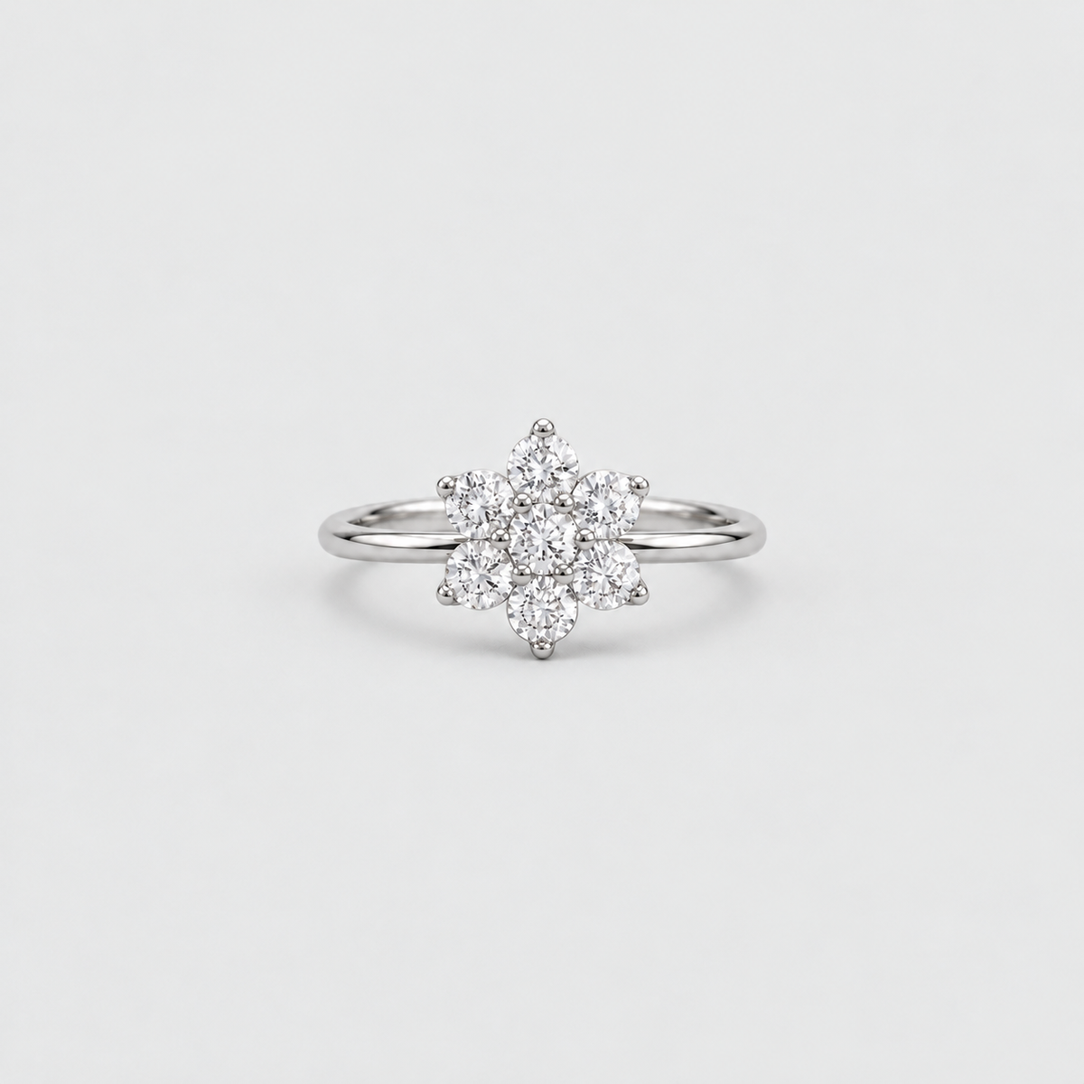 A silver-toned ring featuring a flower-shaped cluster of small clear gemstones on a plain light gray background.