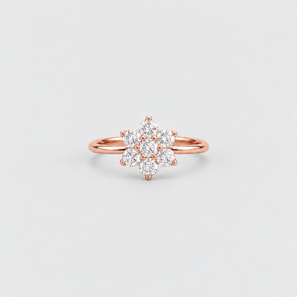 A rose gold ring with a flower-shaped cluster of clear gemstones, photographed on a clean, light gray background.
